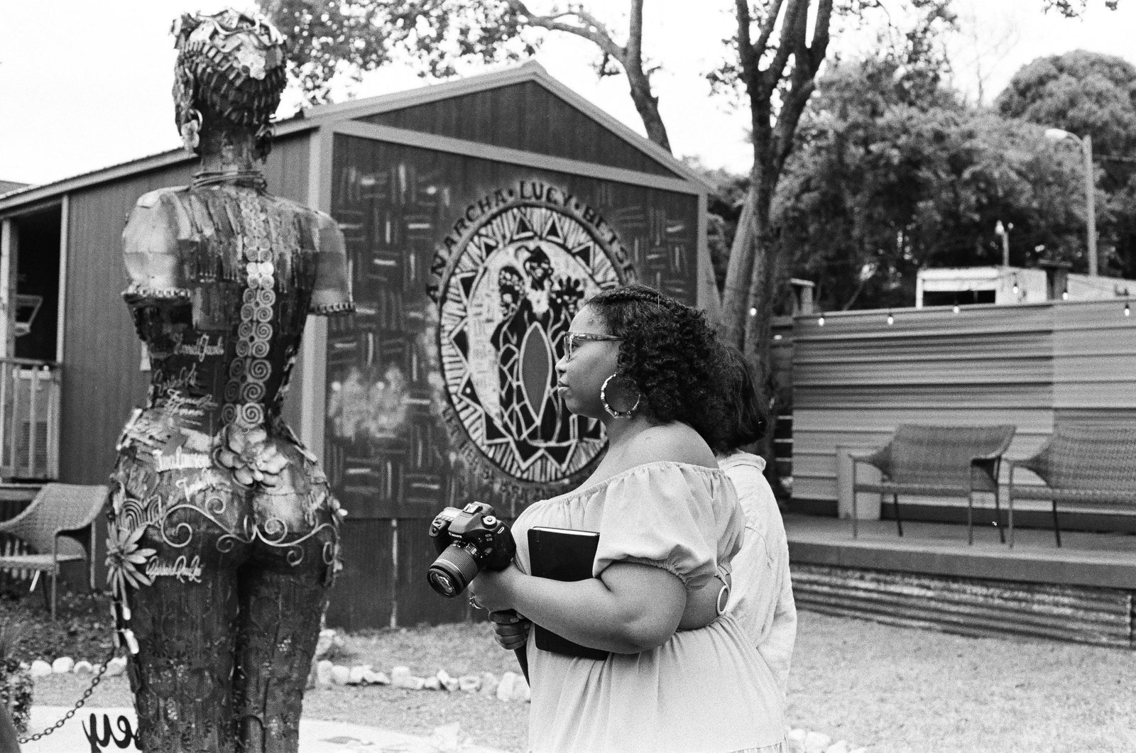 A visitor holding a camera and notebook faces a mural reading Anarcha, Lucy, Betsey, beside the back of one of the sculptures.